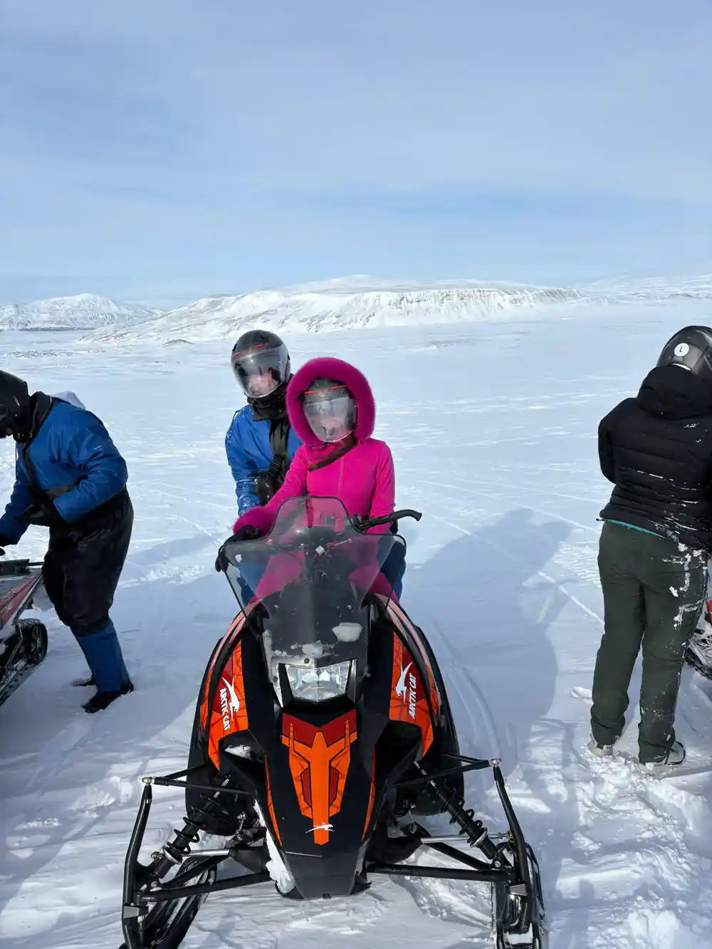 Child on orange snowmobile with adults on snowy glacier