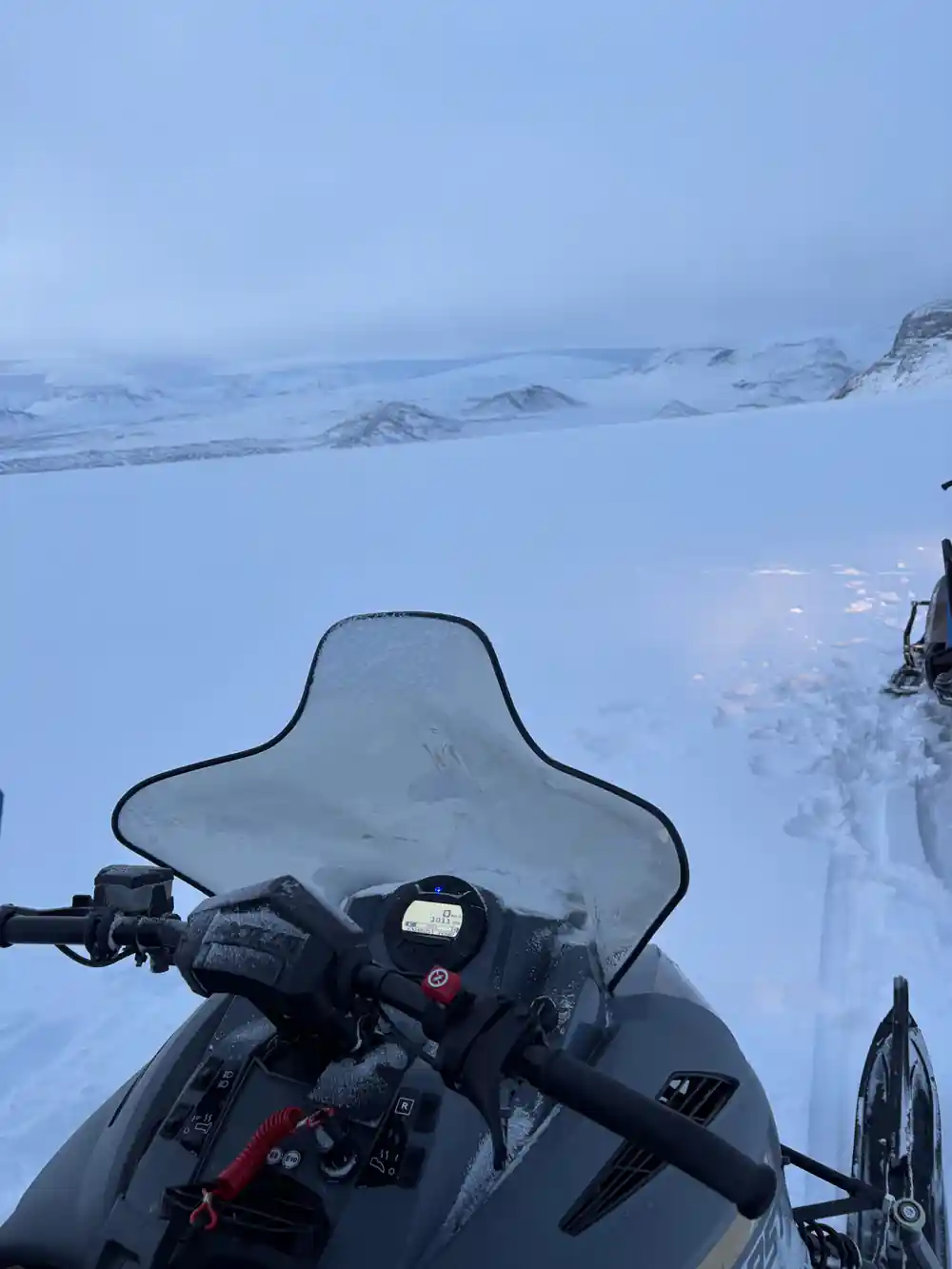 First-person view from snowmobile handlebars over snowy landscape