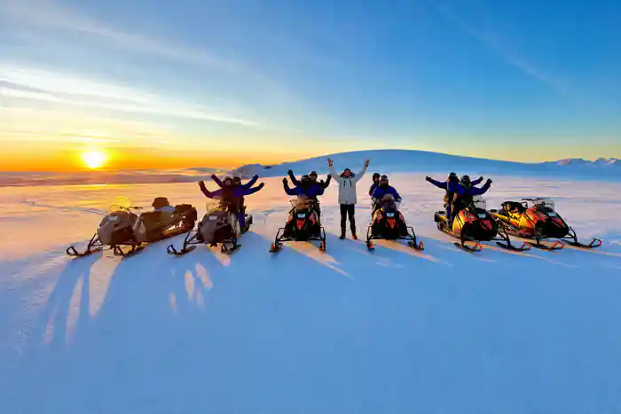 Group celebrating on snowmobiles at frozen lake sunset