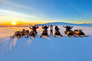 Group celebrating on snowmobiles at frozen lake sunset