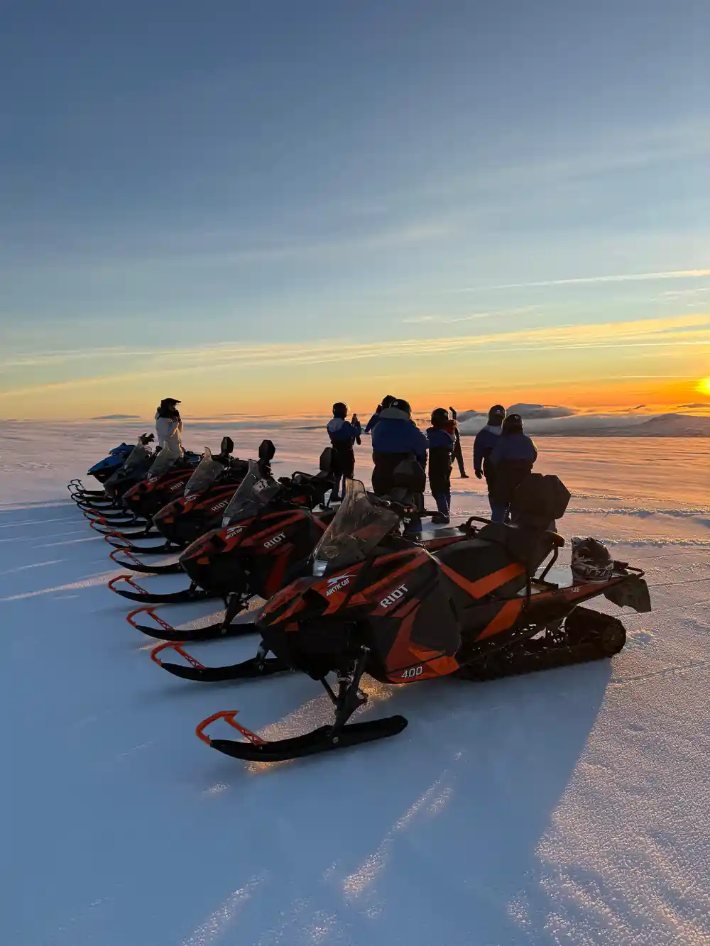 Group of people gathered around snowmobiles at sunset