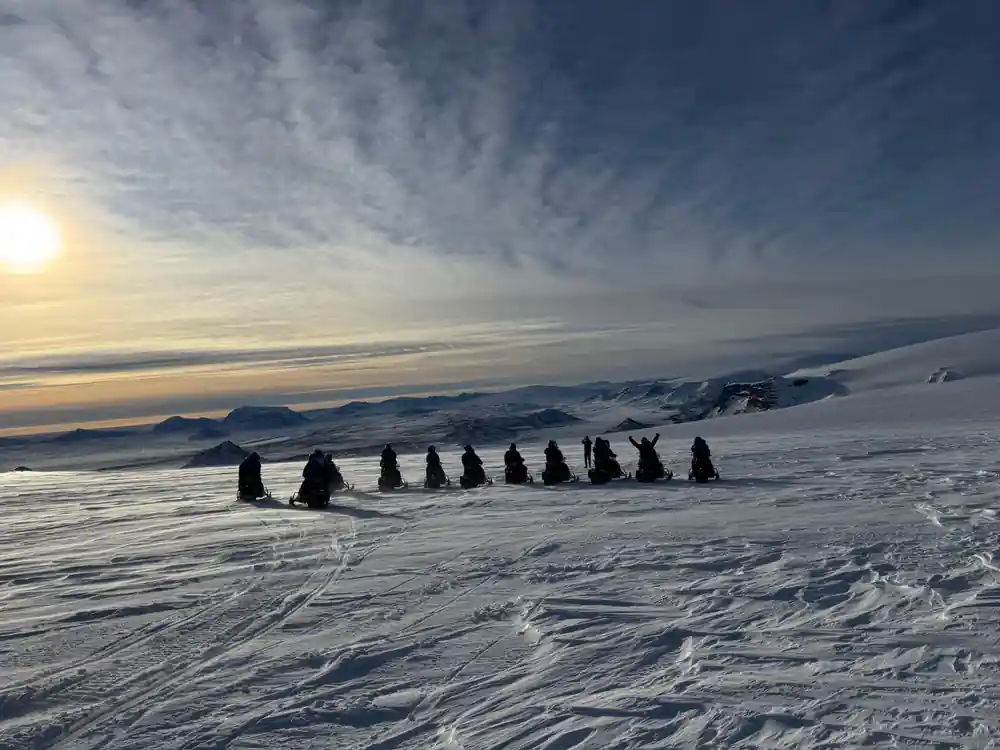 Line of people standing on snow with mountains at sunrise