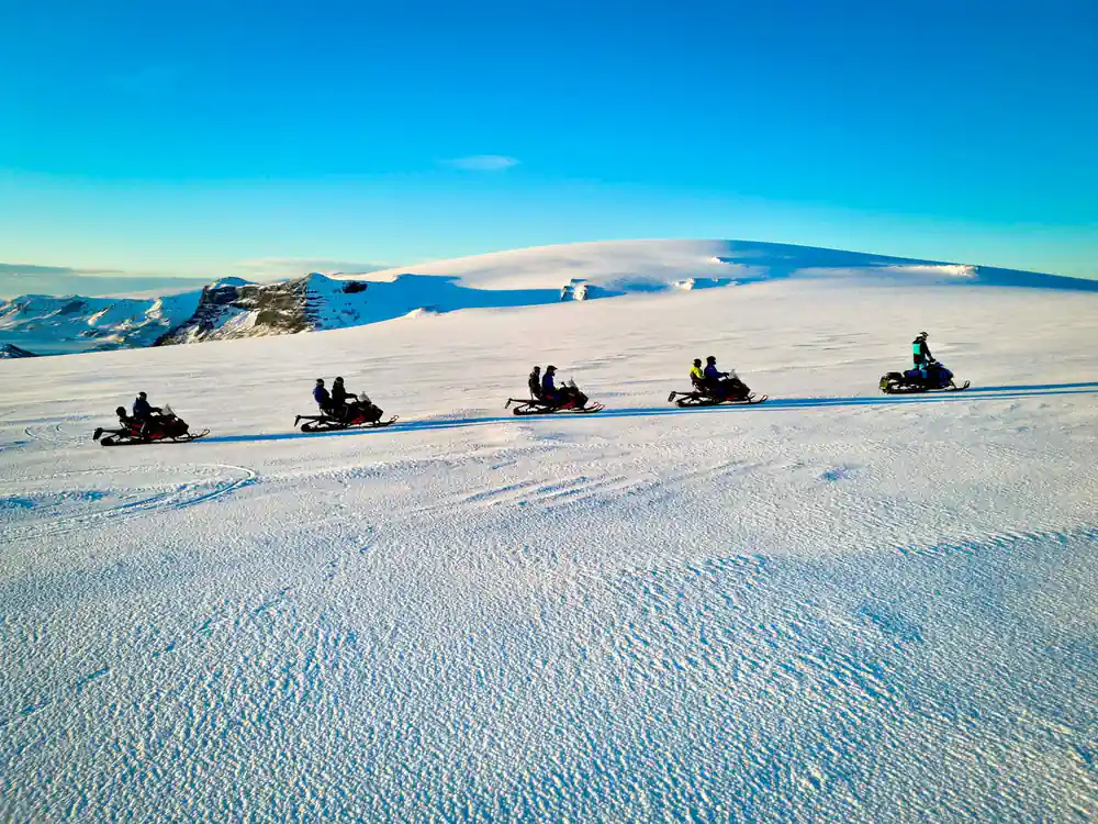 Line of snowmobiles traveling across frozen expanse
