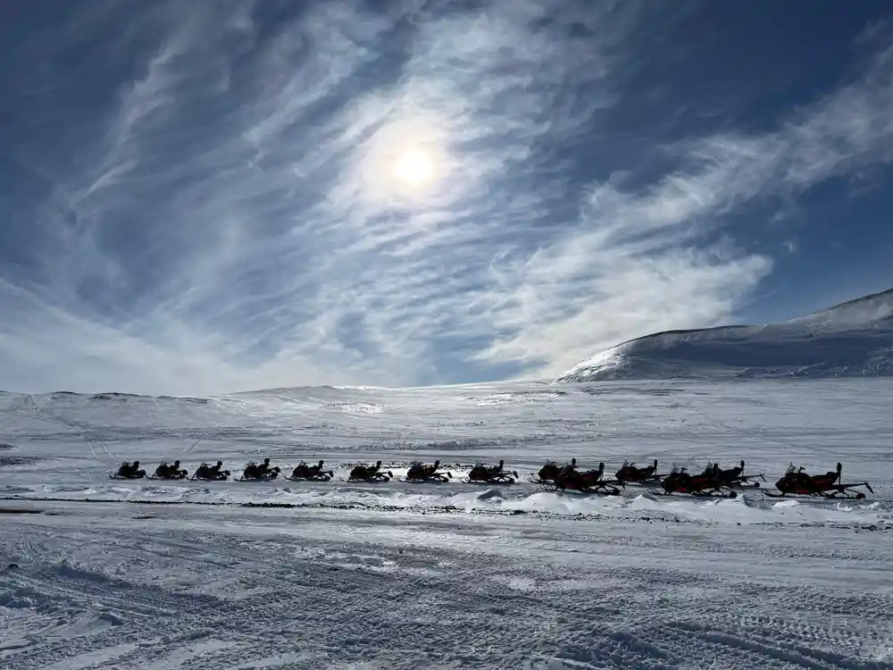 Long line of people on snowmobiles across frozen lake