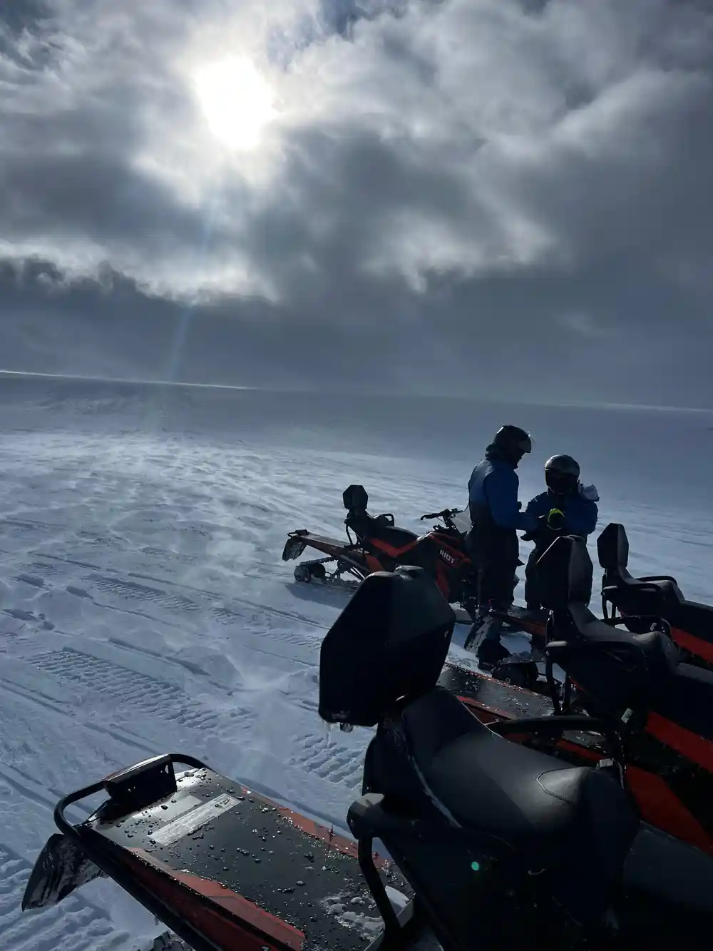 Multiple snowmobiles parked on frozen lake with people