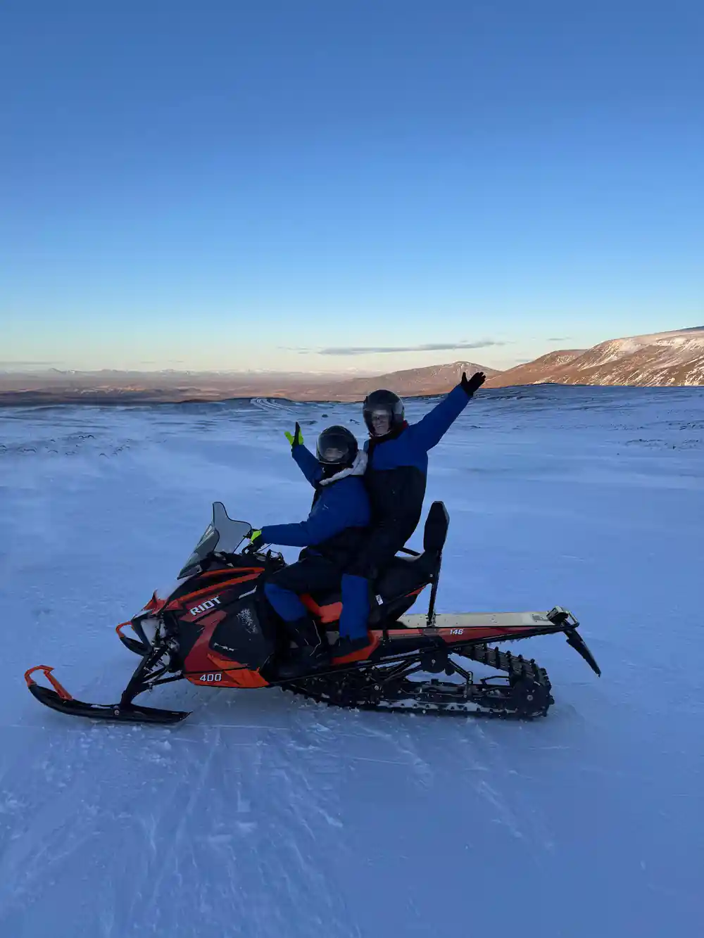 Person on snowmobile with raised arm at sunset