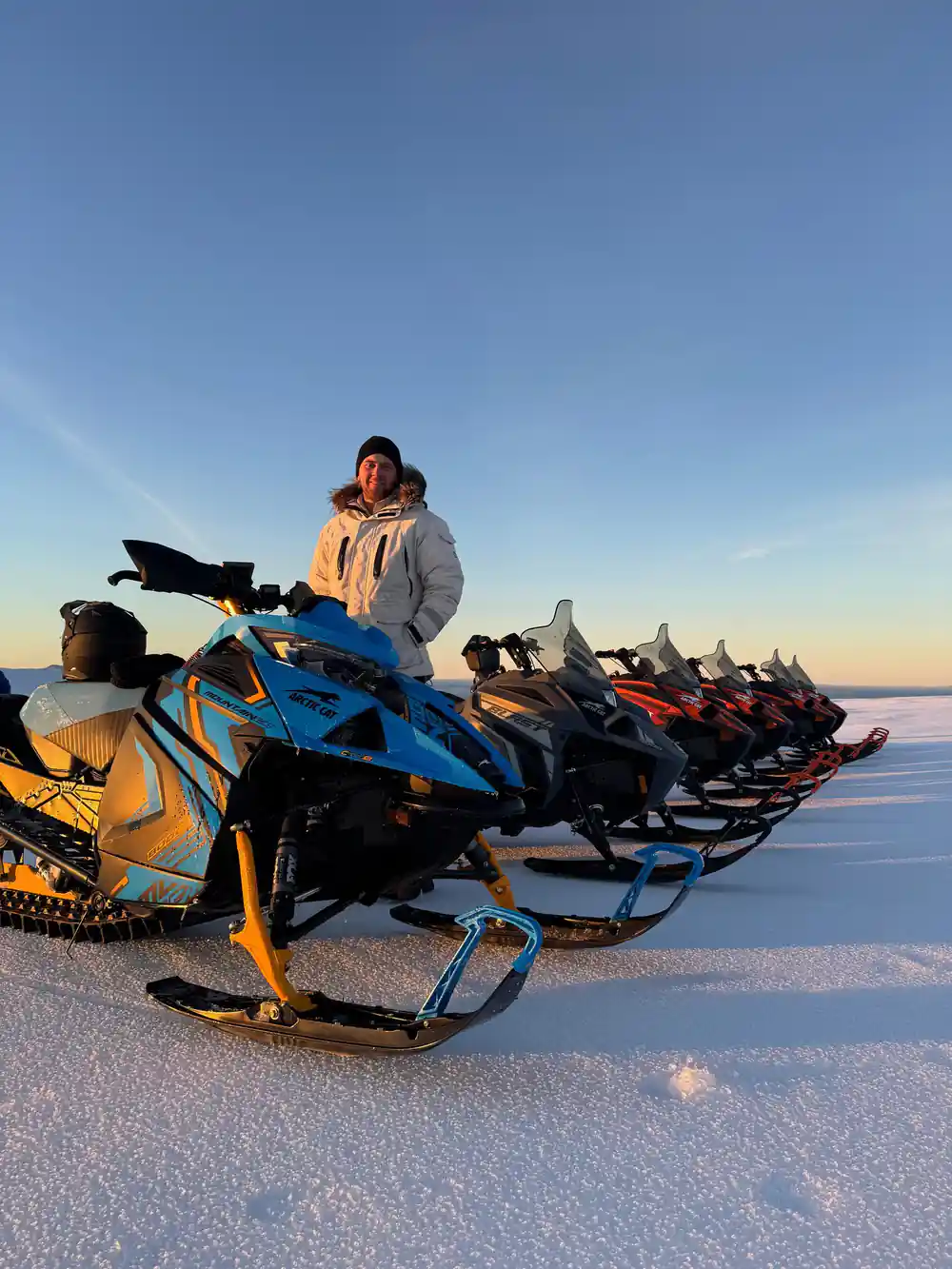 Row of snowmobiles lined up on frozen lake at dusk