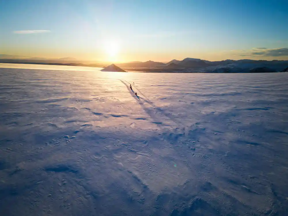 Single person standing on vast frozen lake at sunset