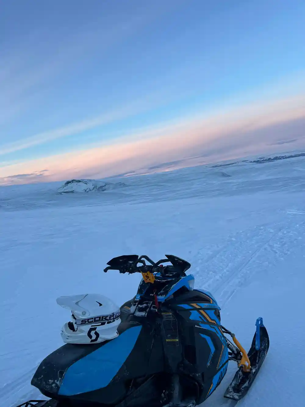 Snowmobile on frozen lake at dusk with distant mountains