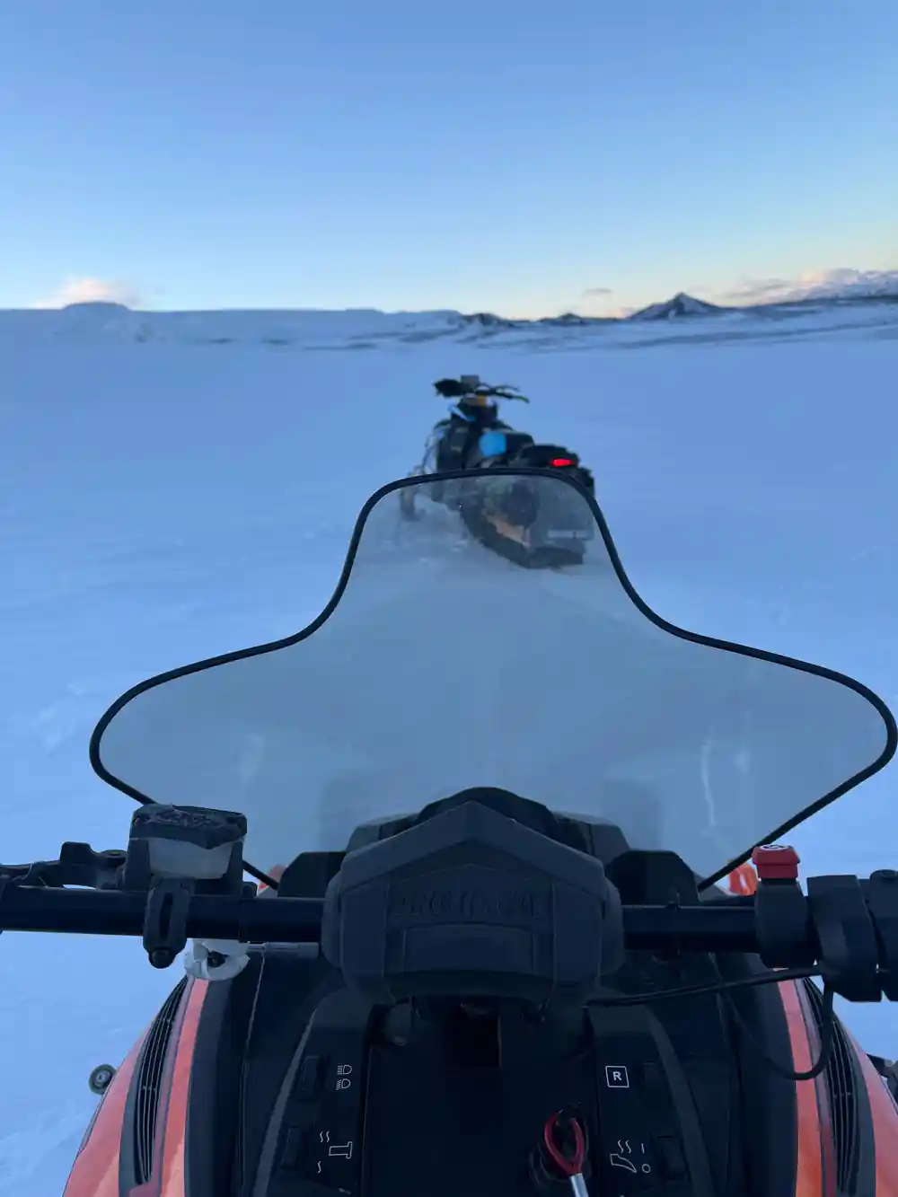Snowmobile windscreen view over snowy plain with distant mountains