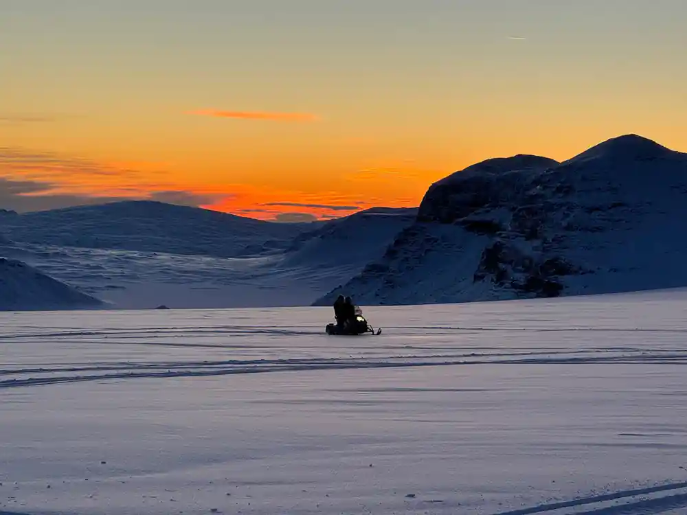 Snowmobiler on frozen lake with mountain silhouette at dusk