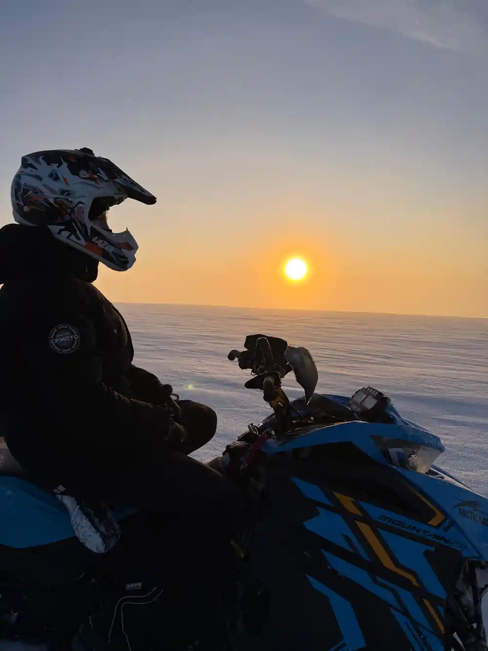 Snowmobiler in helmet on frozen lake at sunrise