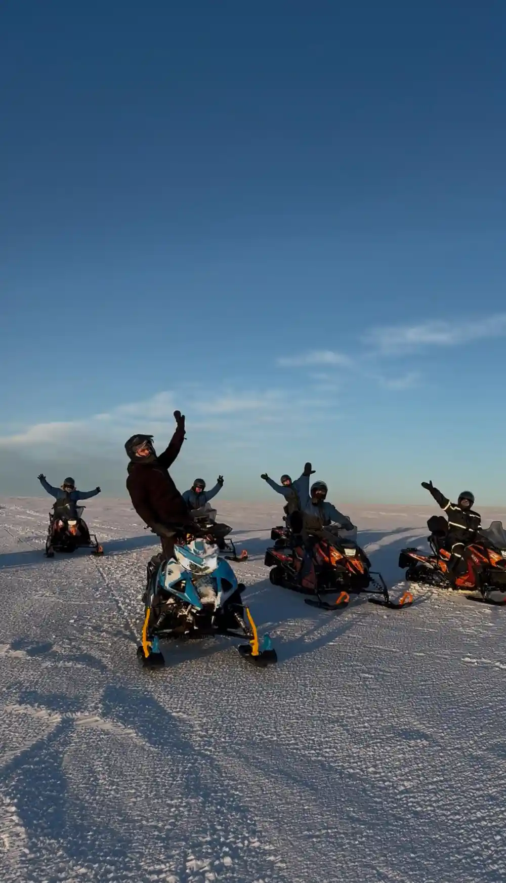 Snowmobilers gathered on frozen lake with mountains at sunset