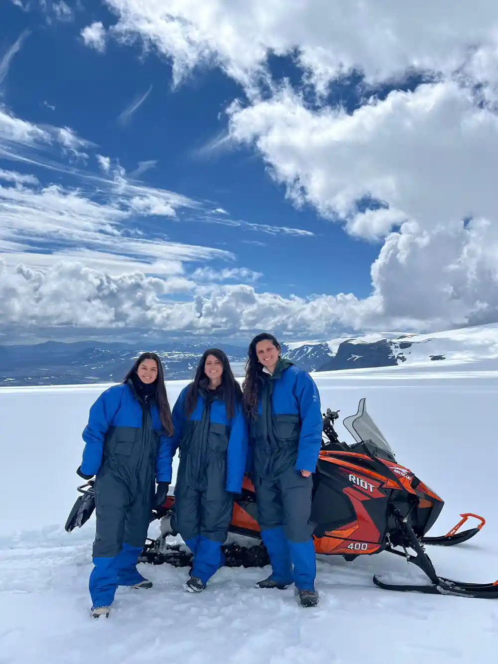 Three people in blue winter suits beside orange snowmobile