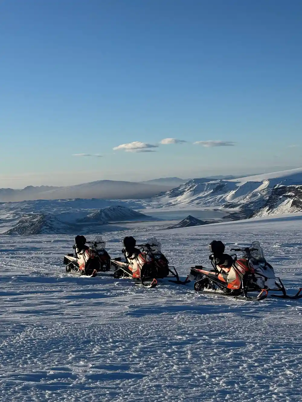 Three snowmobiles parked on snow with mountain backdrop