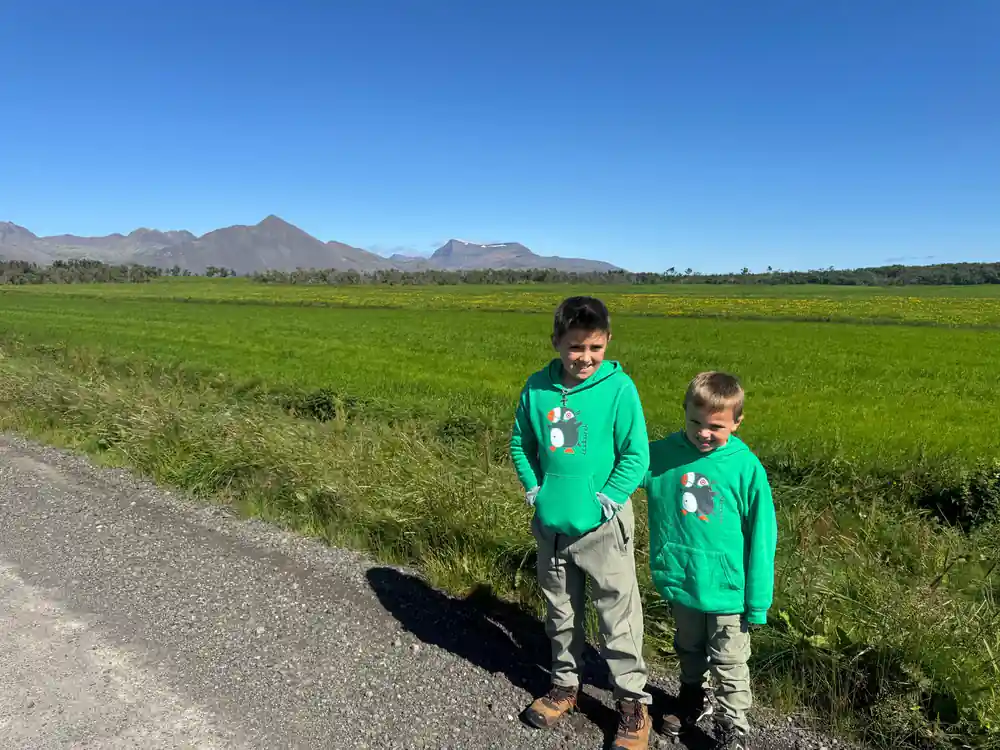 Two children in green jackets standing in green valley with mountains