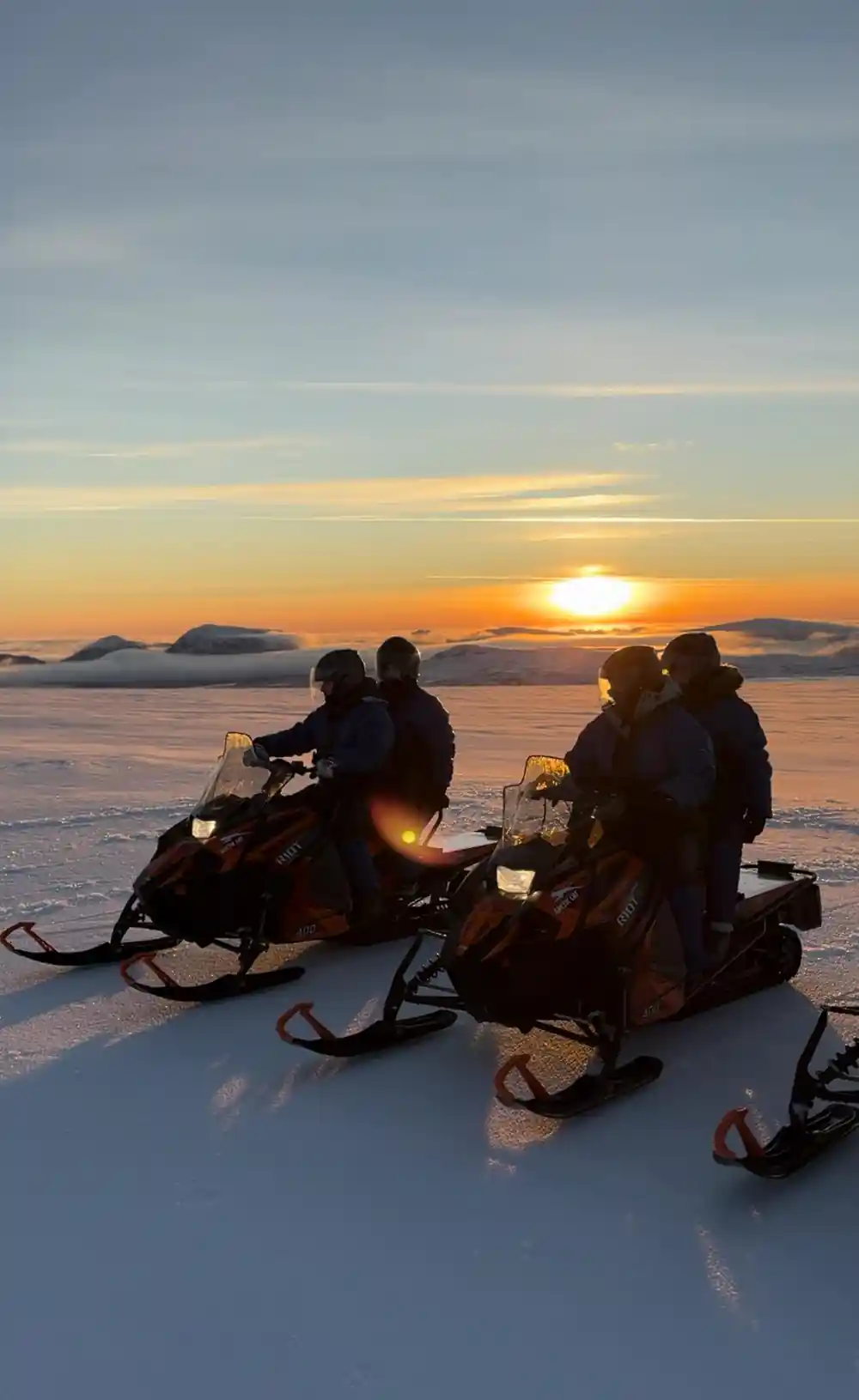 Two couples on snowmobiles at sunset on frozen landscape