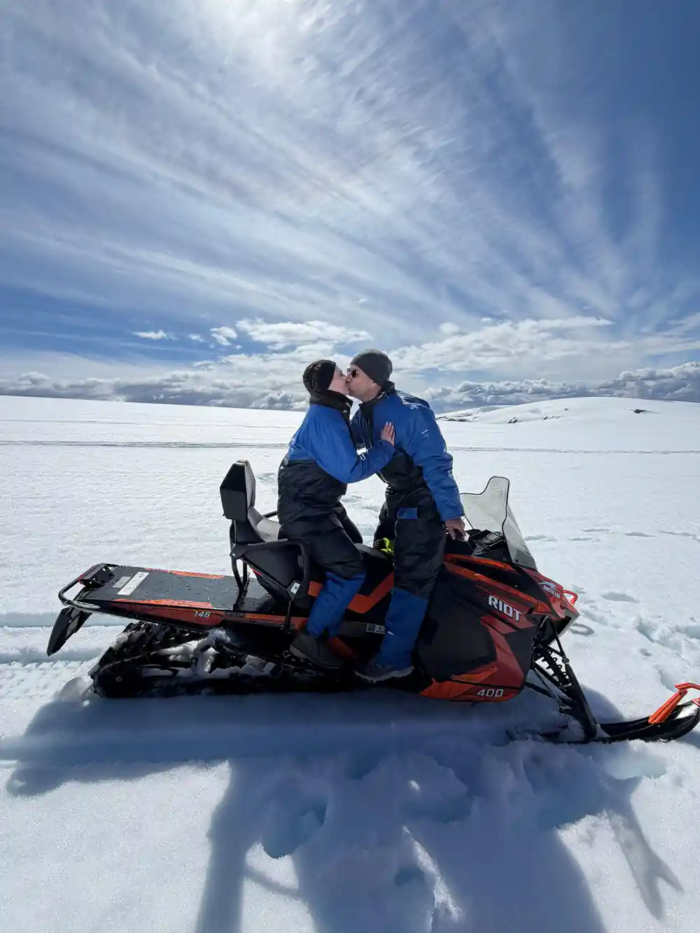 Two people kissing on red snowmobile in snowy landscape