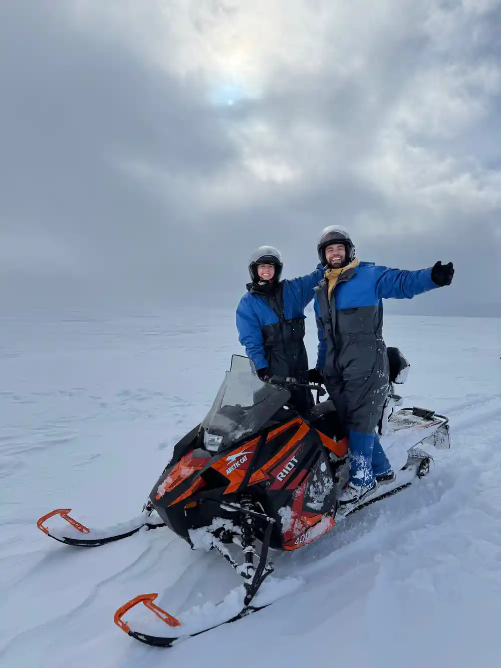 Two people on red snowmobile in snowy landscape waving
