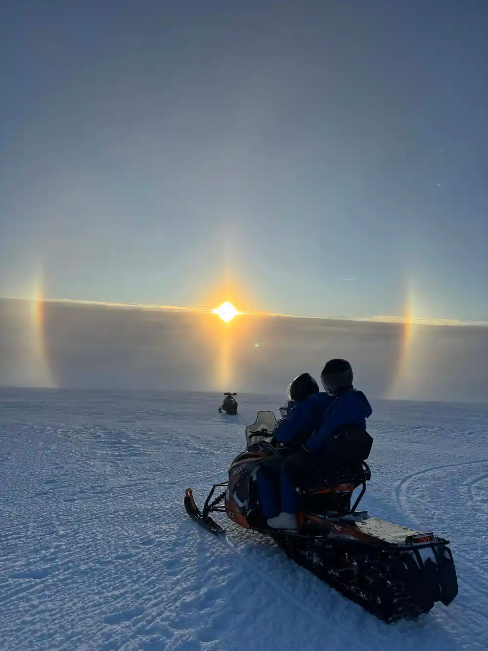Two people sitting on snowmobile with sun dogs effect