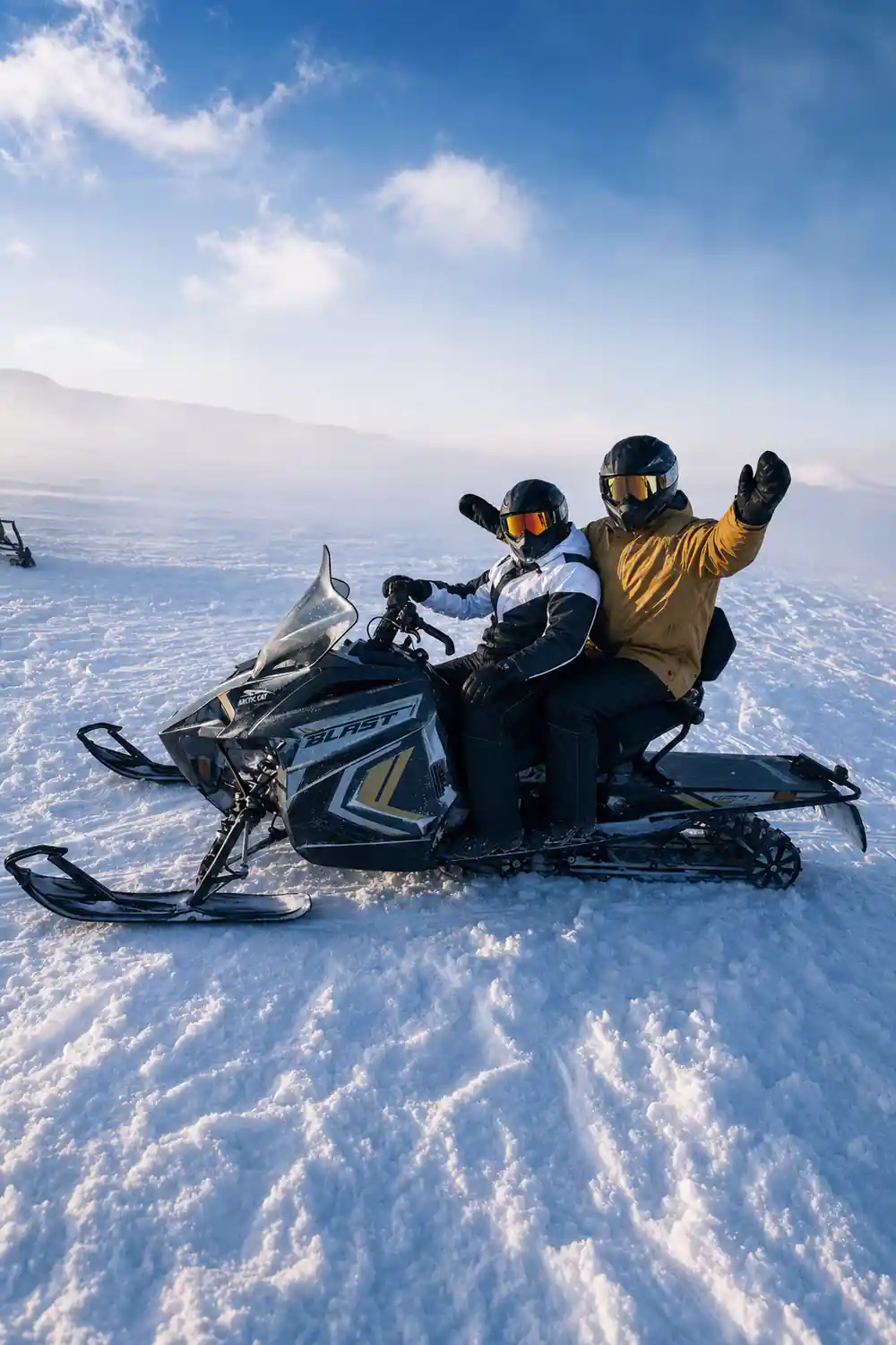 Two people on snowmobile raising arms in snow