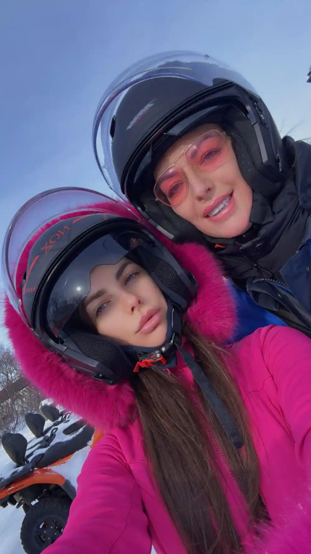 Two people wearing helmets smiling at camera outdoors