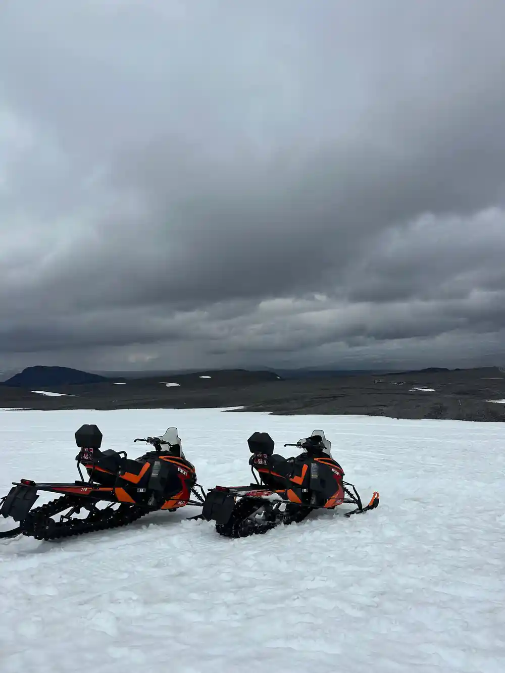 Two snowmobiles parked on glacier with dramatic cloudy sky