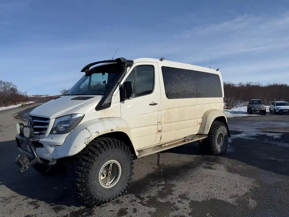 White modified van with large tires parked on gravel