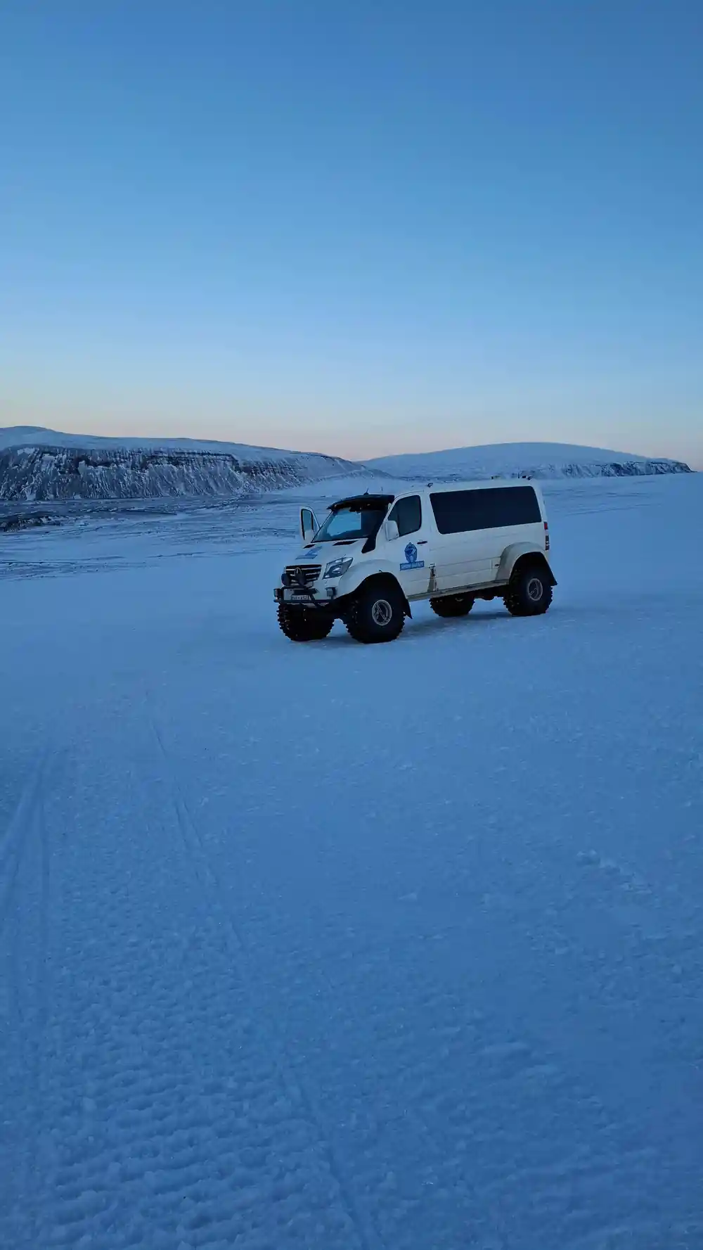 White van parked on vast frozen lake with mountain backdrop