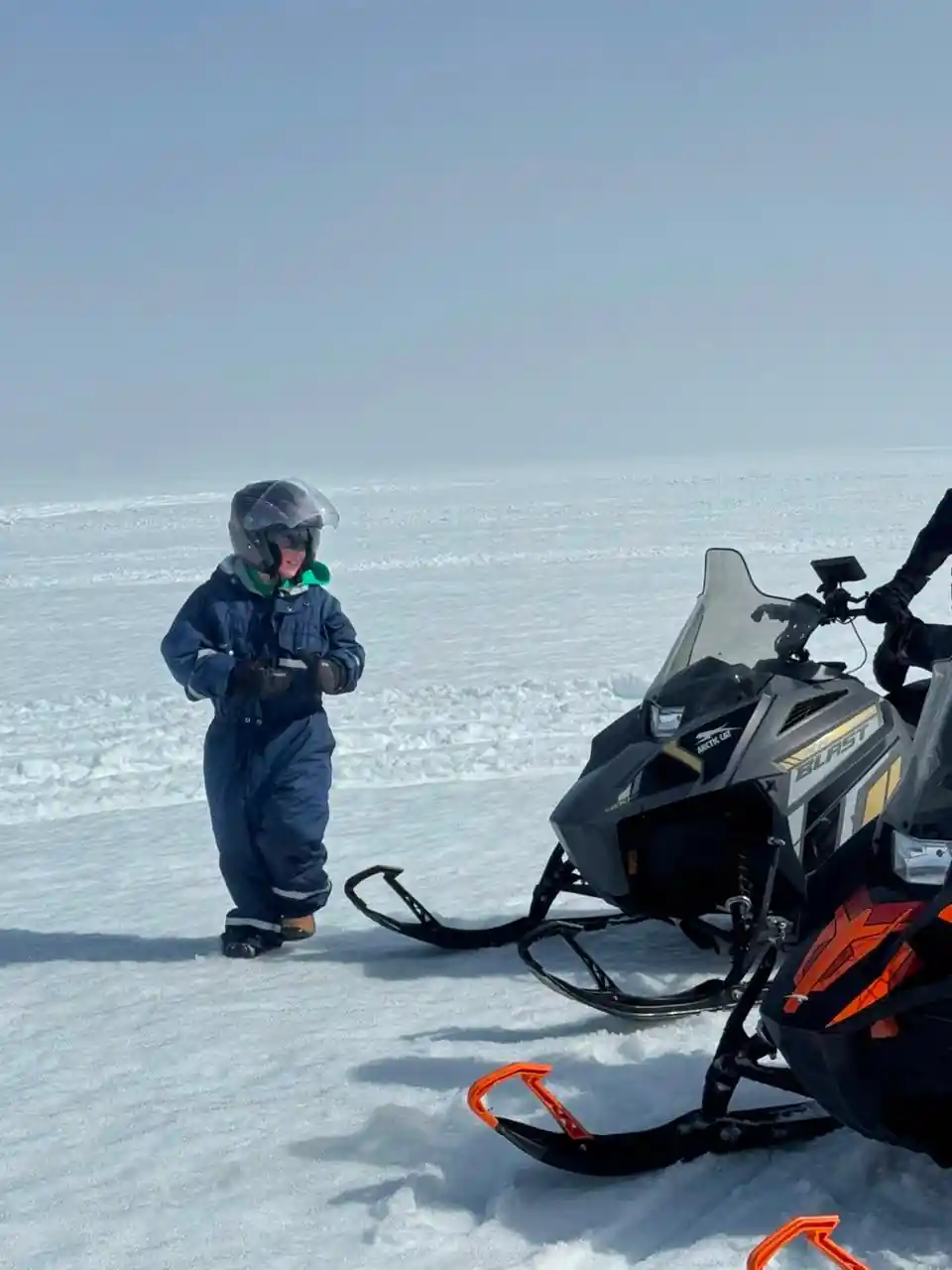 Young child standing beside snowmobile on ice
